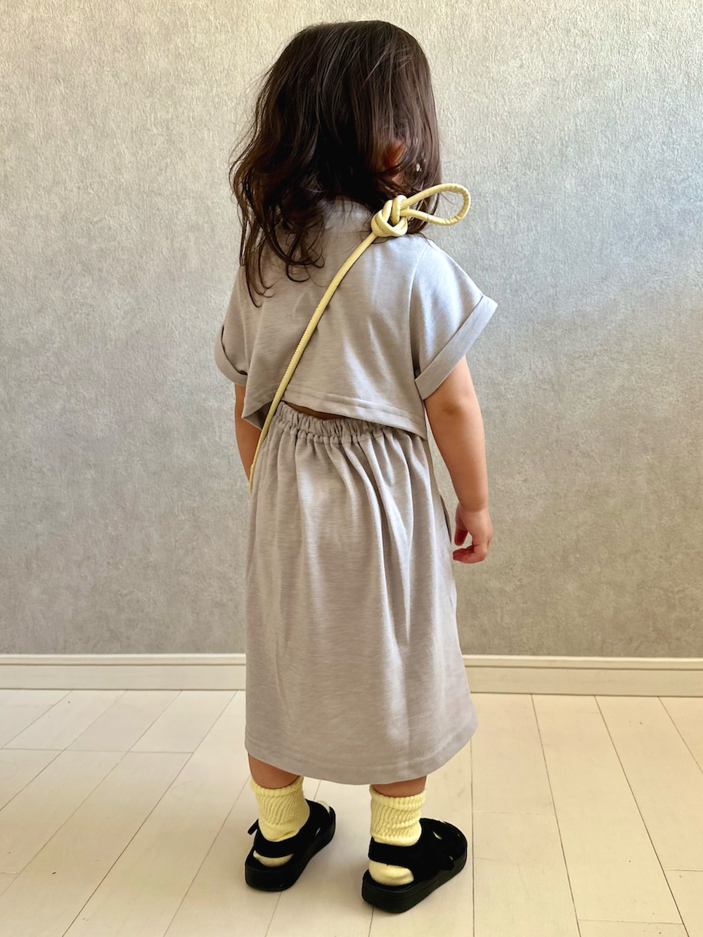 グレー系のワンピース、イエロー系のショルダーバッグ、ブラック系のサンダルを着用したキッズの夏コーディネートの2枚目の写真