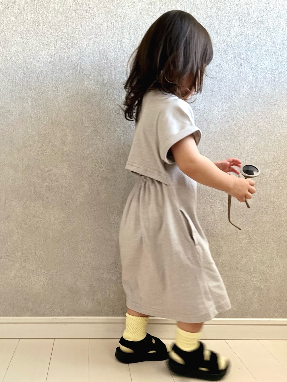 グレー系のワンピース、イエロー系のショルダーバッグ、ブラック系のサンダルを着用したキッズの夏コーディネートの3枚目の写真