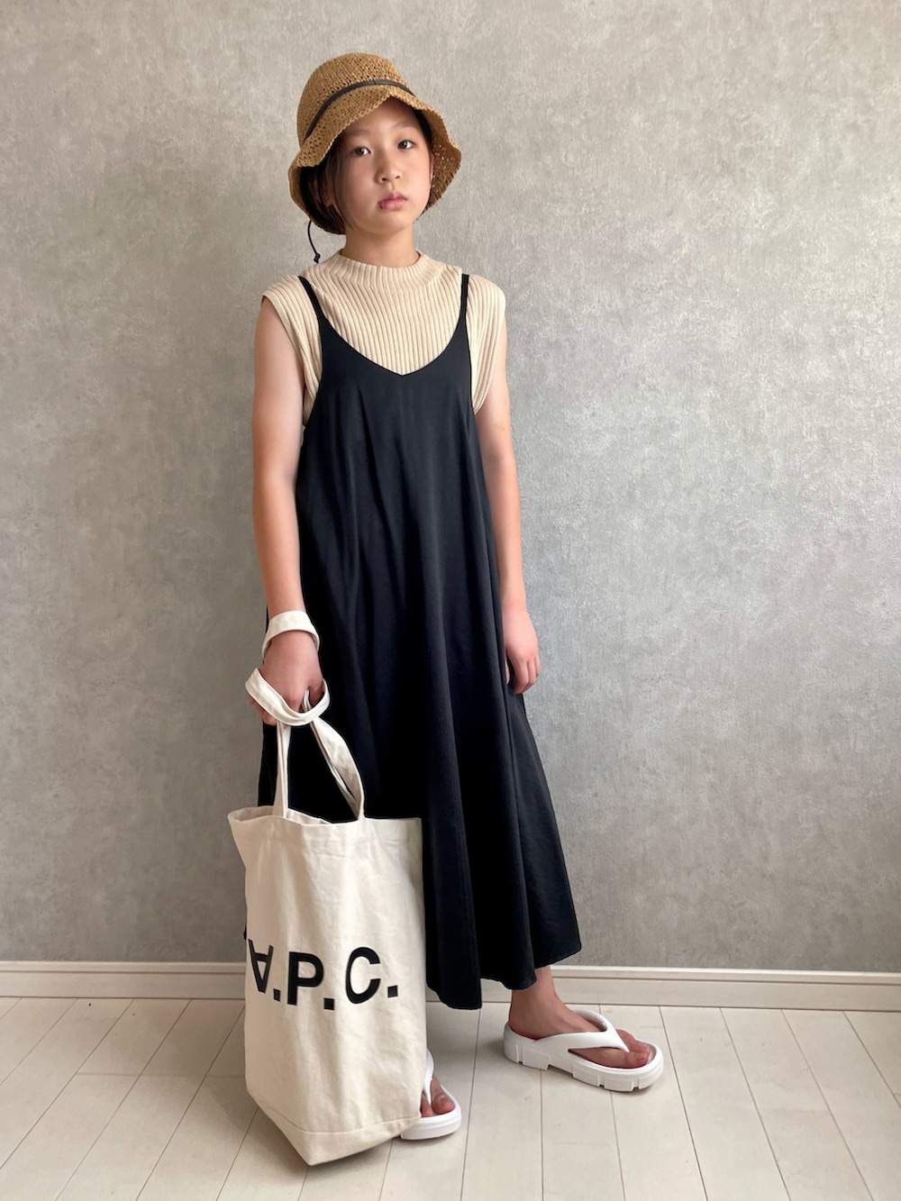 ベージュ系のTシャツ/カットソー、ブラック系のジャンパースカート、ホワイト系のトートバッグを着用したキッズの夏コーディネートの2枚目の写真