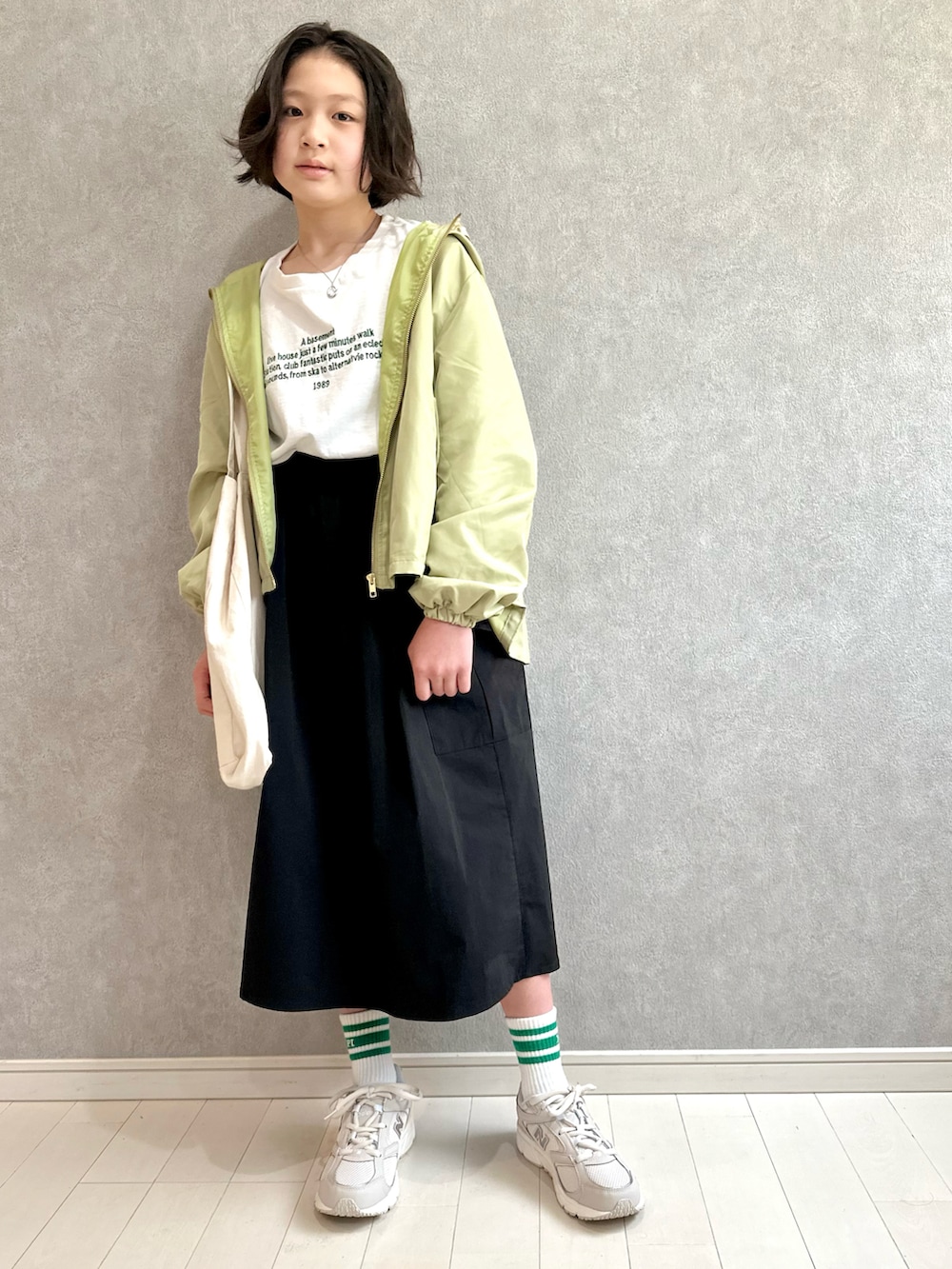 グリーン系のマウンテンパーカー、ホワイト系のTシャツ/カットソー、ブラック系のスカートを着用したキッズの春コーディネートの2枚目の写真