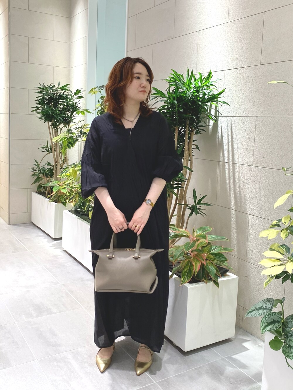 ブラック系のワンピース、ベージュ系のハンドバッグ、ゴールド系のパンプスを着用したレディースの夏コーディネートの2枚目の写真