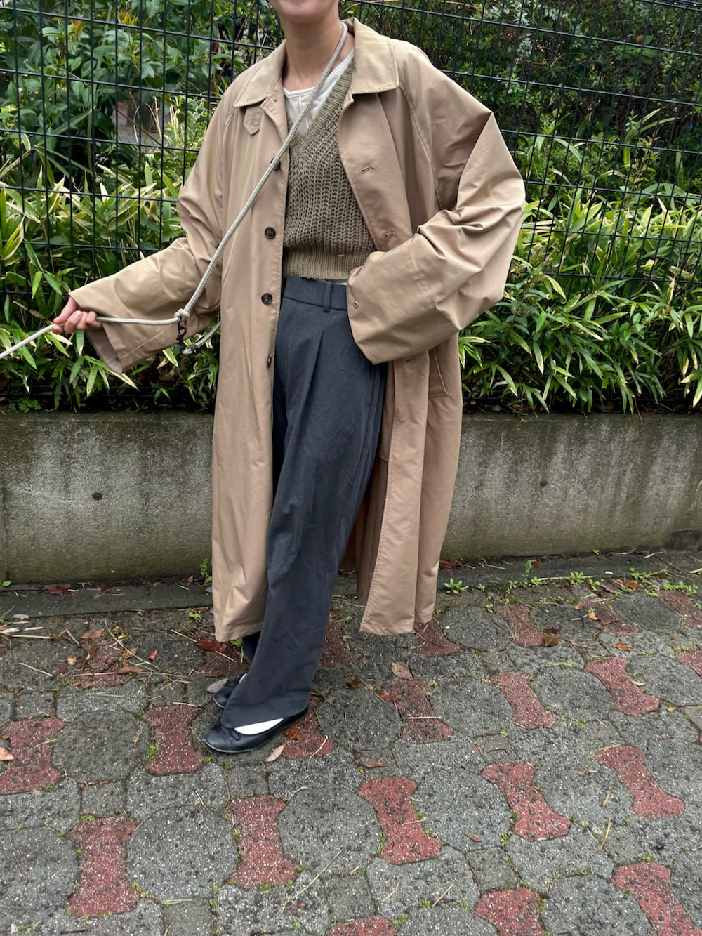 ベージュ系のステンカラーコート、グリーン系のベスト、ブラック系のバレエシューズを着用したレディースの春コーディネートの2枚目の写真