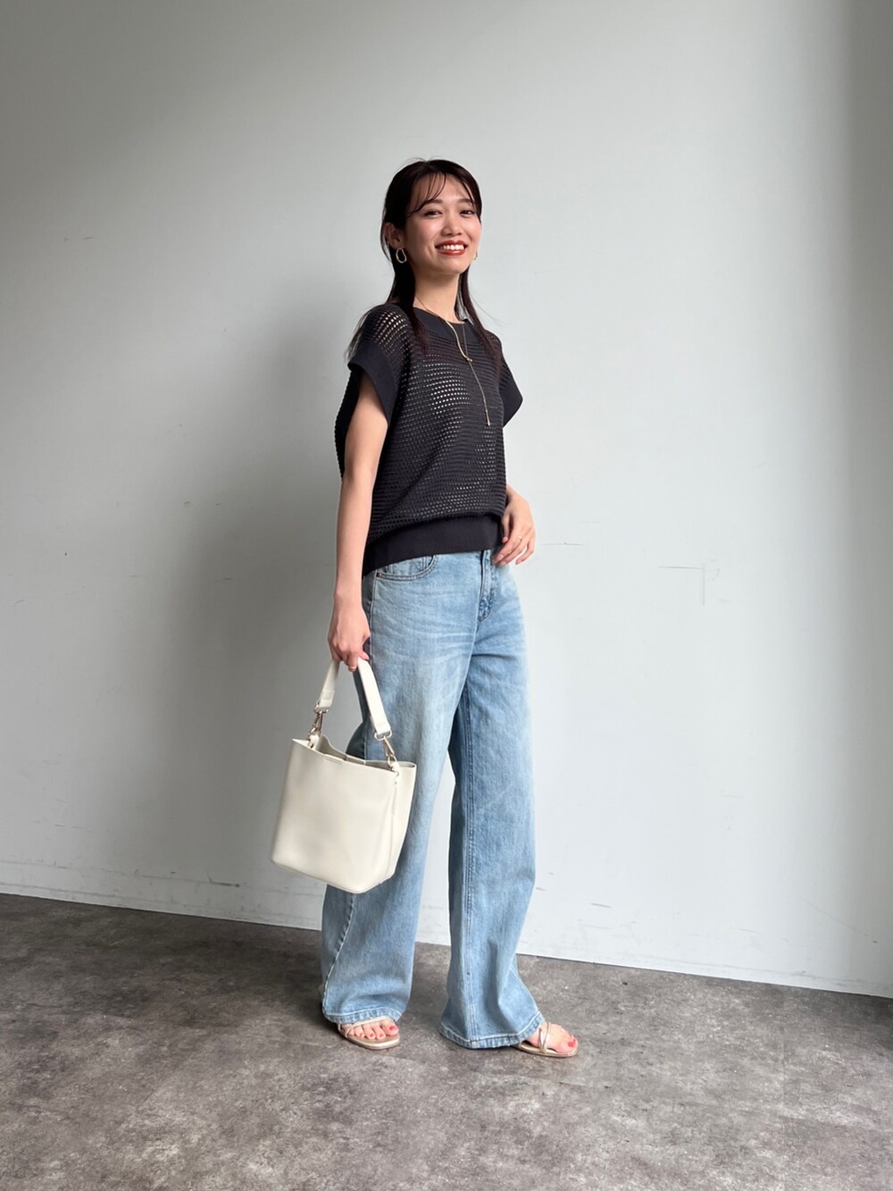 グレー系のニット/セーター、ブルー系のデニムパンツ、ホワイト系のショルダーバッグを着用したレディースの夏コーディネートの3枚目の写真