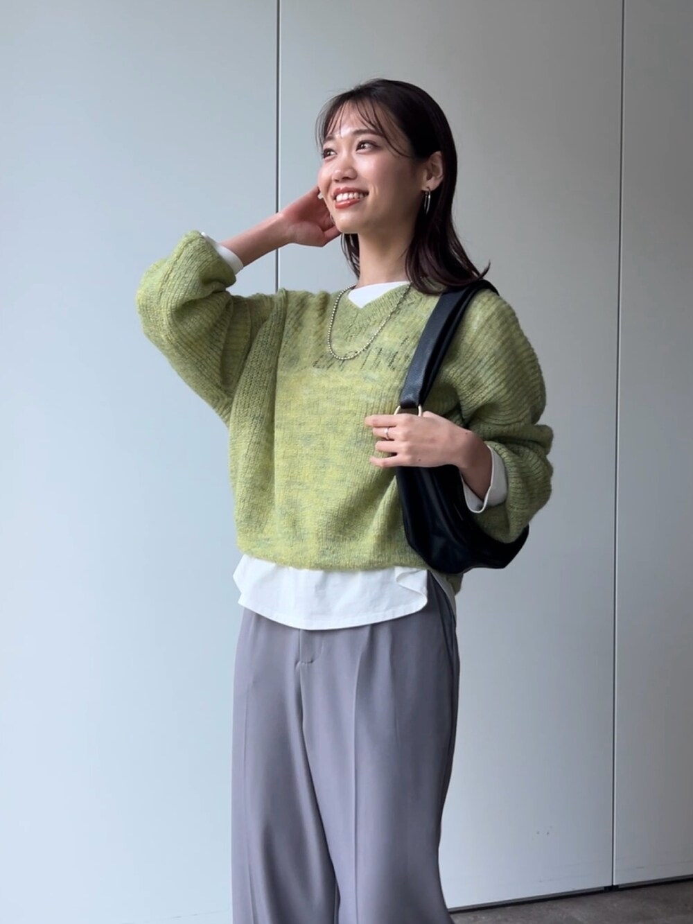 グリーン系のニット/セーター、ホワイト系のTシャツ/カットソー、ブラック系のショルダーバッグを着用したレディースの冬コーディネートの2枚目の写真