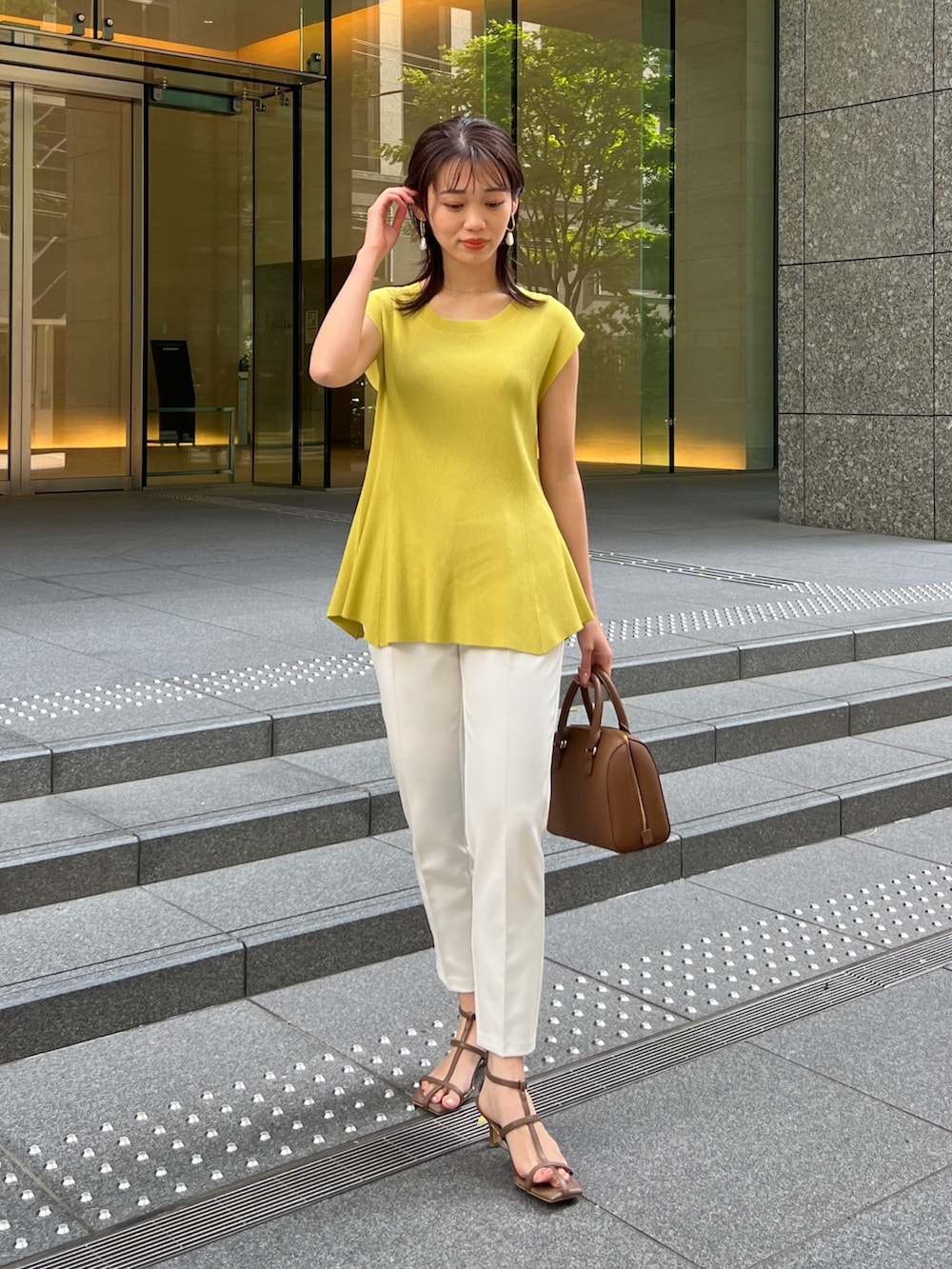 イエロー系のニット/セーター、ブラウン系のサンダル、ホワイト系のパンツを着用したレディースの春コーディネートの2枚目の写真