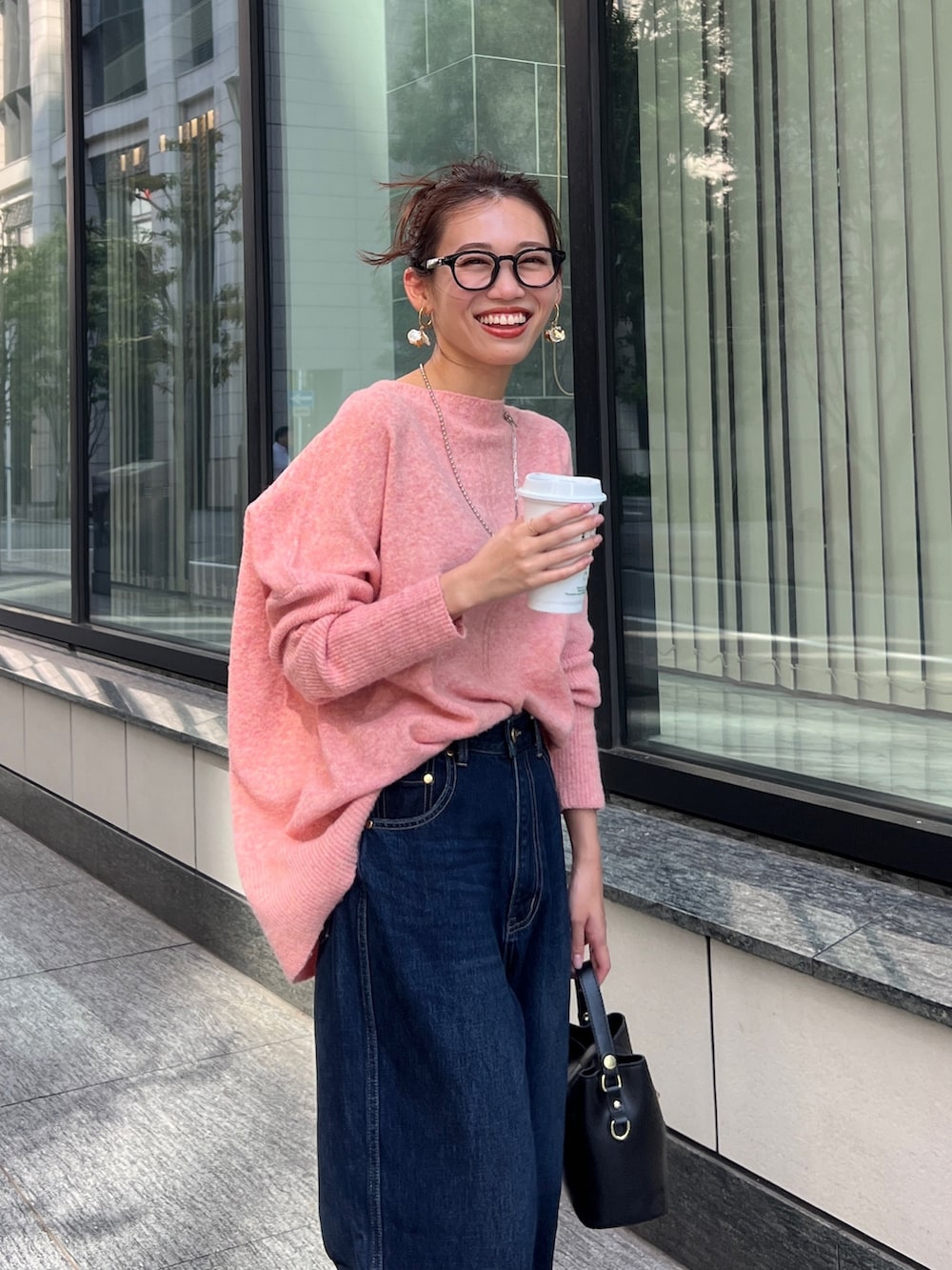 オレンジ系のニット/セーター、ブラック系のショルダーバッグ、ブルー系のデニムパンツを着用したレディースの秋コーディネートの3枚目の写真