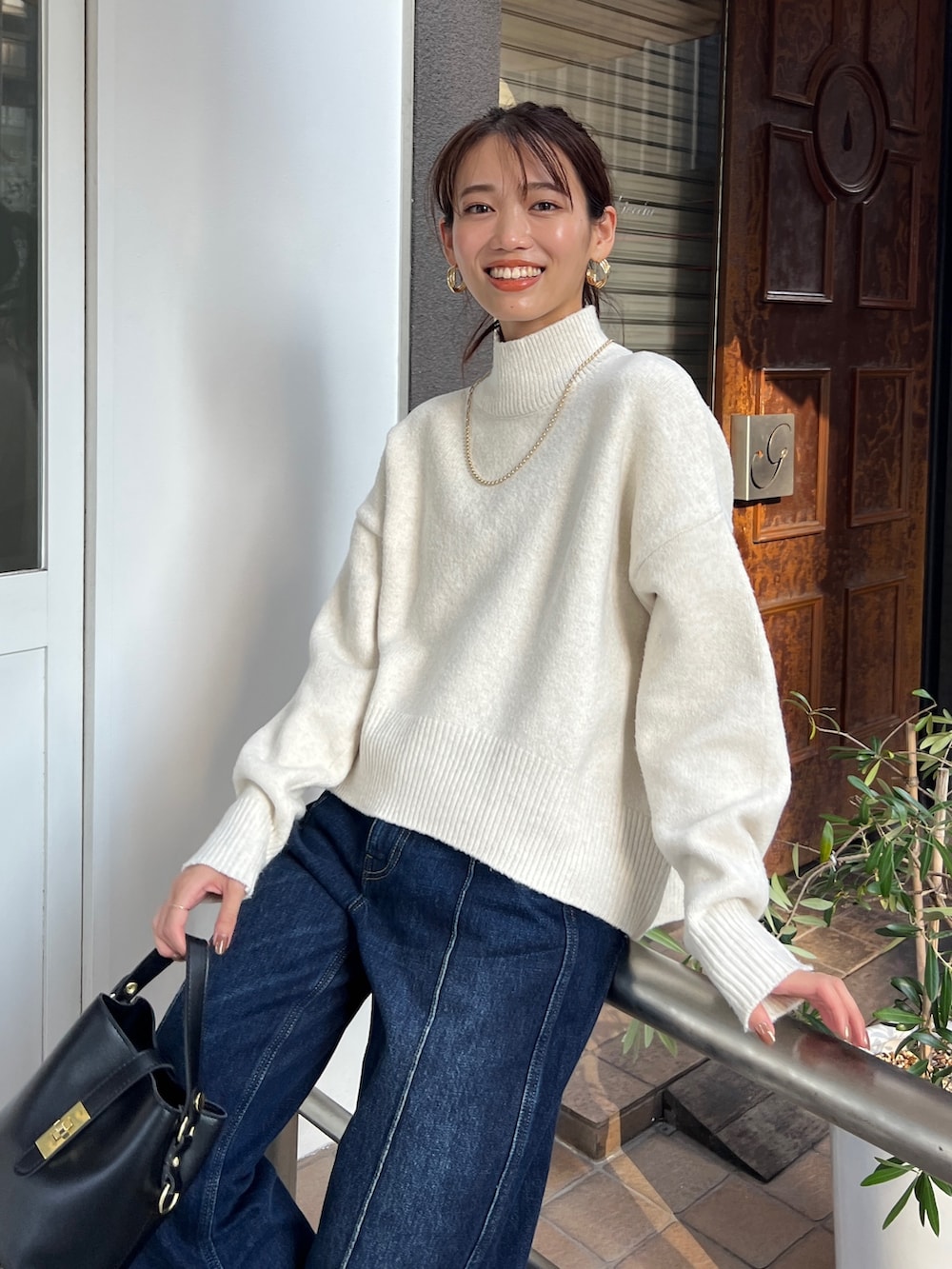 ホワイト系のニット/セーター、ブルー系のデニムパンツ、ブラック系のショルダーバッグを着用したレディースの秋コーディネートの2枚目の写真