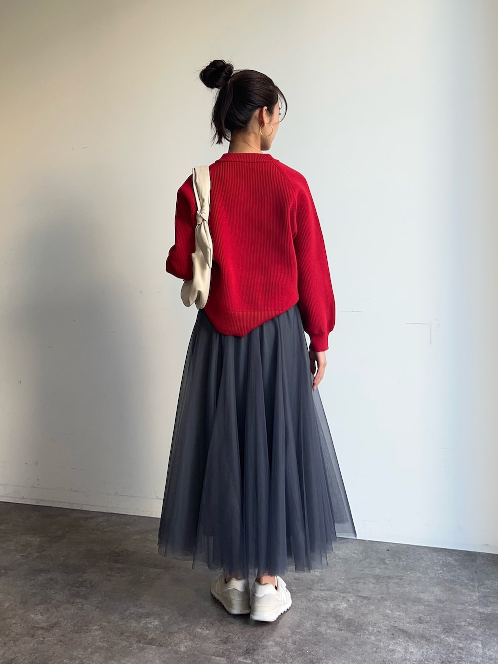 レッド系のニット/セーター、ホワイト系のショルダーバッグ、グレー系のスカートを着用したレディースの冬コーディネートの2枚目の写真