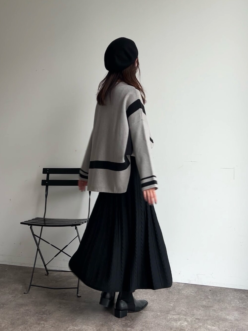 グレー系のニット/セーター、ブラック系のスカート、ブラック系のブーツを着用したレディースの冬コーディネートの2枚目の写真