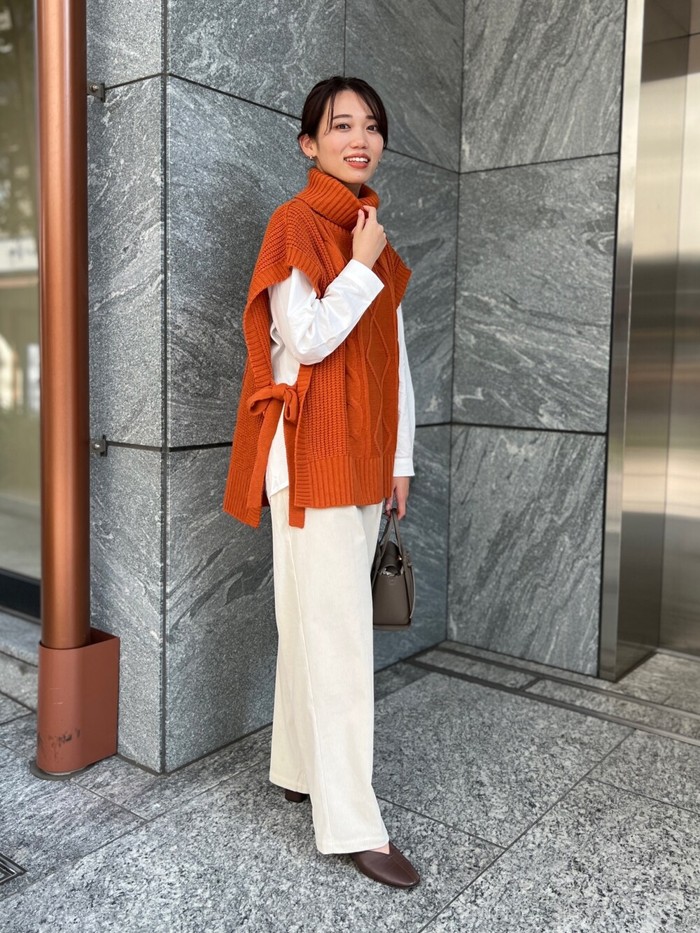 ホワイト系のパンツ、オレンジ系のベスト、ホワイト系のシャツ/ブラウスを着用したレディースの秋コーディネートの2枚目の写真