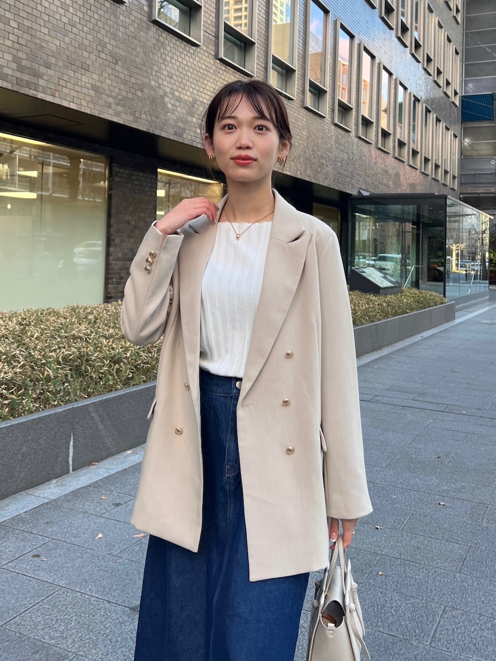 ベージュ系のテーラードジャケット、ブルー系のデニムスカート、グレー系のショルダーバッグを着用したレディースの冬コーディネートの2枚目の写真