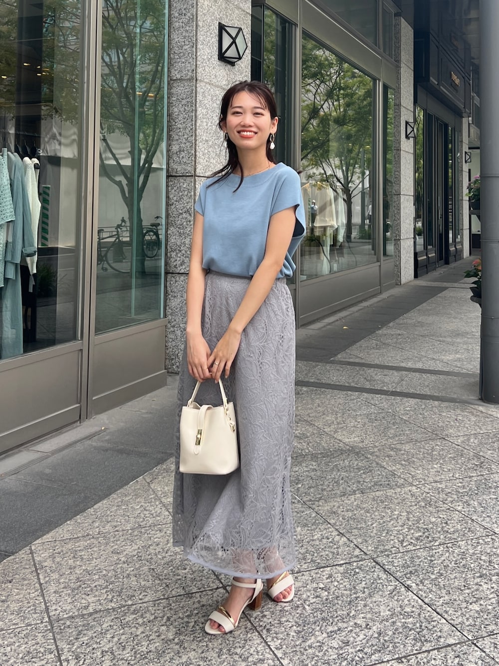 ブルー系のニット/セーター、グレー系のスカート、ホワイト系のショルダーバッグを着用したレディースの夏コーディネートの2枚目の写真