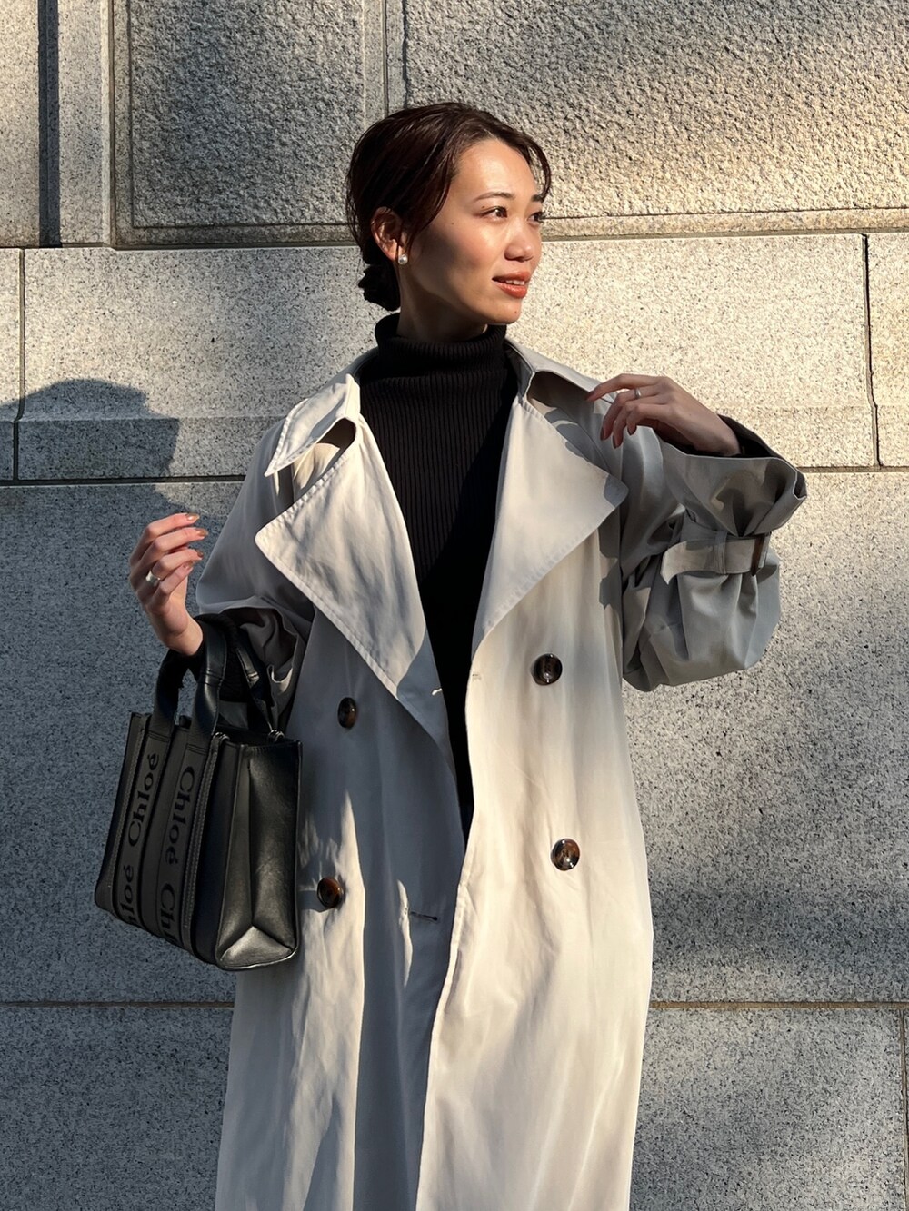 ベージュ系のトレンチコート、ブルー系のスカート、ブラック系のニット/セーターを着用したレディースの冬コーディネートの2枚目の写真