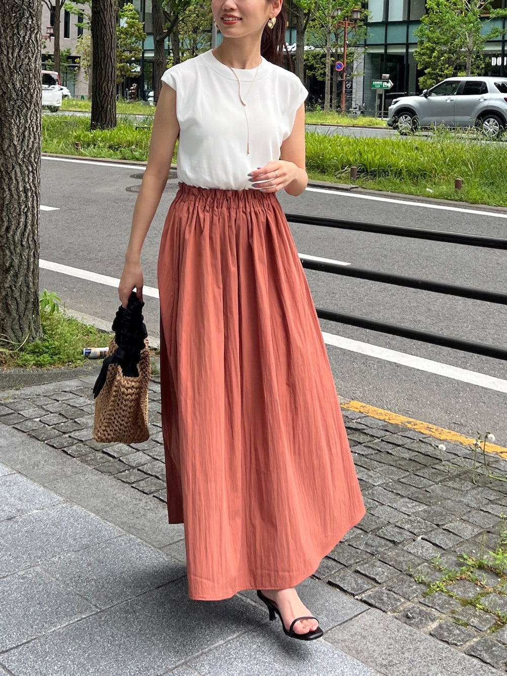 オレンジ系のワンピース、ブラック系のかごバッグ、シルバー系のシューズを着用したレディースの春コーディネートの2枚目の写真