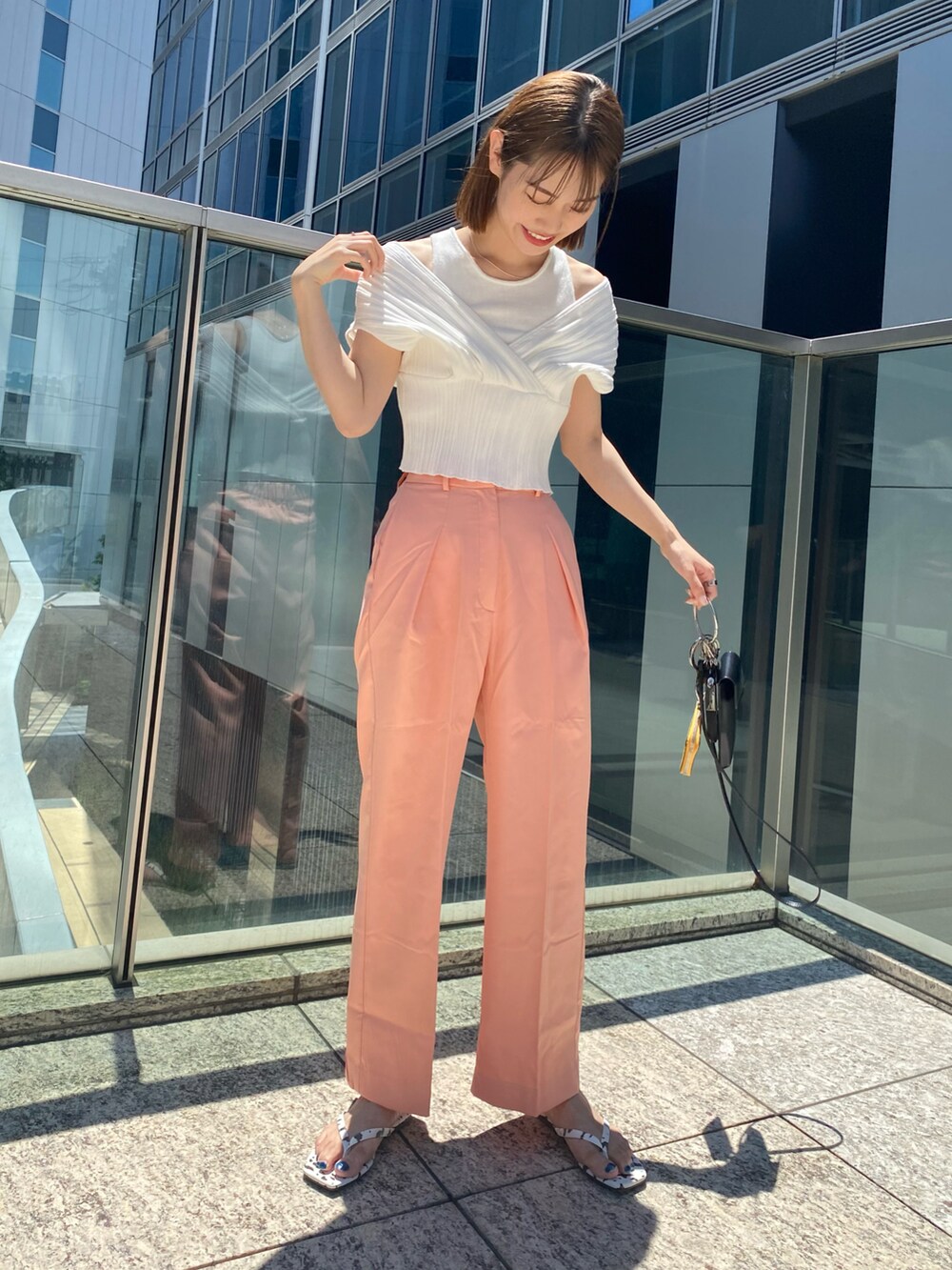 ホワイト系のニット/セーター、オレンジ系のスラックス、ブラック系のトートバッグを着用したレディースの夏コーディネートの2枚目の写真