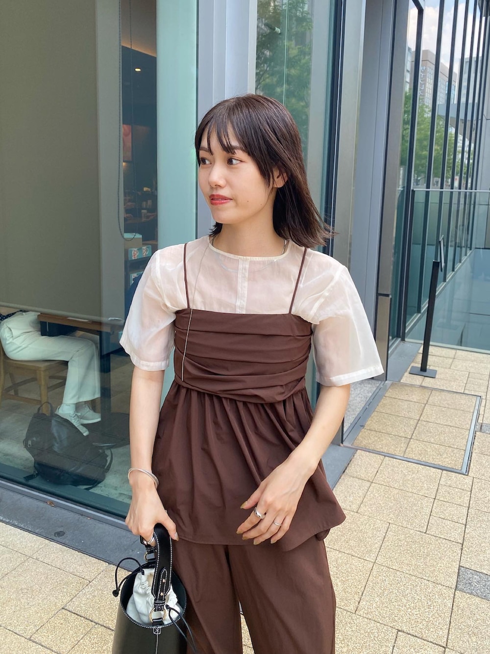 ブラック系のハンドバッグ、ブラウン系のトップス、ホワイト系のシャツ/ブラウスを着用したレディースの夏コーディネートの2枚目の写真