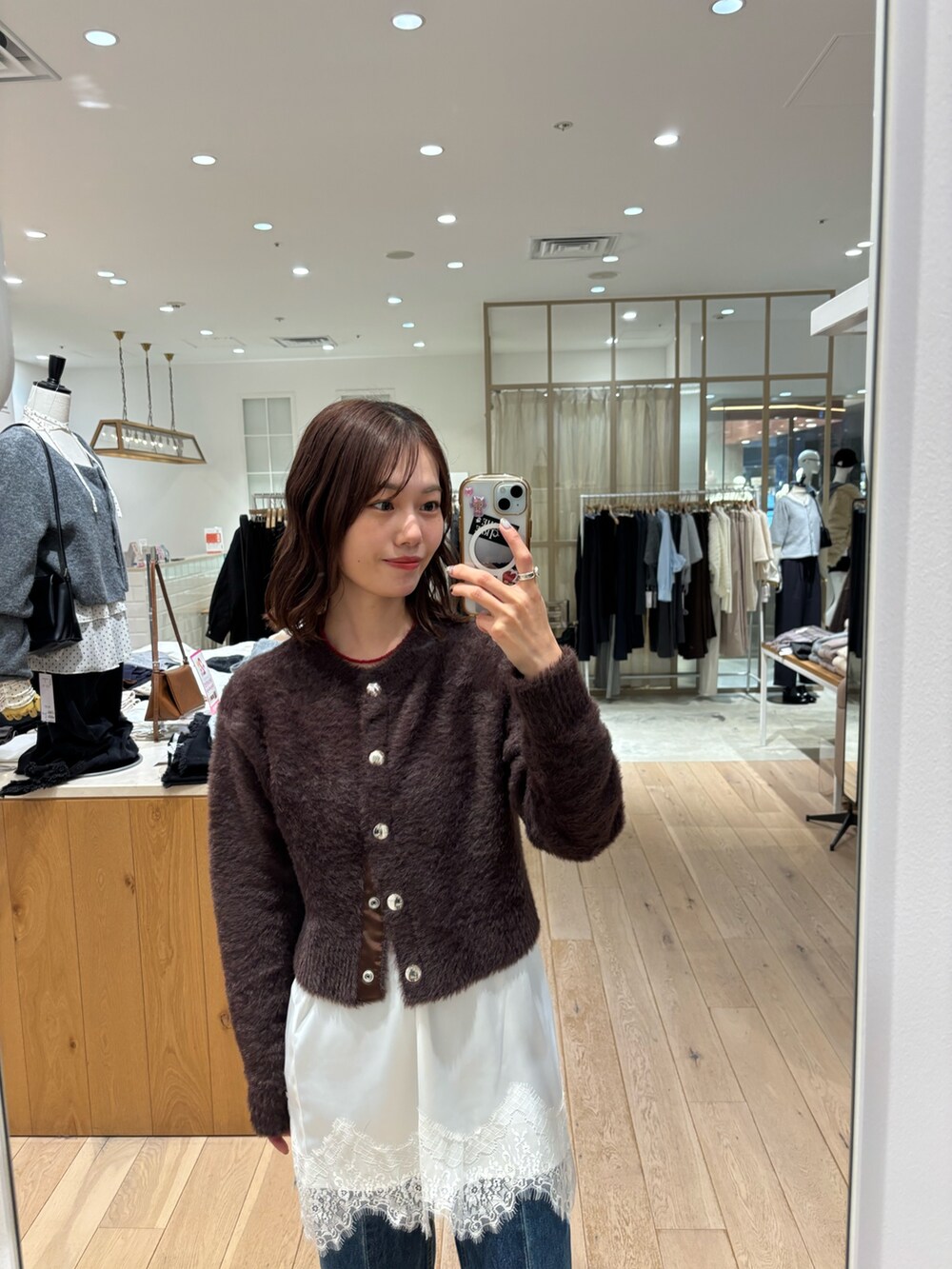 ブルー系のデニムパンツ、ブラウン系のカーディガン/ボレロ、ホワイト系のスカートを着用したレディースの冬コーディネートの2枚目の写真