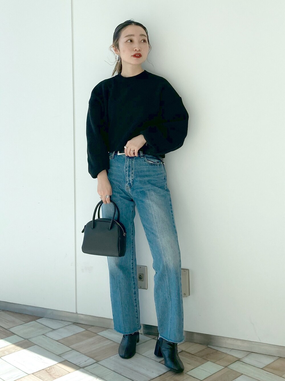 ブルー系のデニムパンツ、ブラック系のニット/セーター、ブラック系のボストンバッグを着用したレディースの冬コーディネートの4枚目の写真