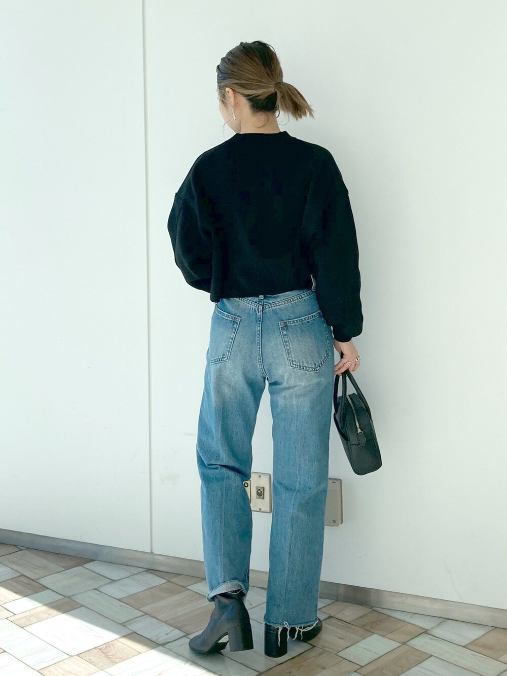 ブルー系のデニムパンツ、ブラック系のニット/セーター、ブラック系のボストンバッグを着用したレディースの冬コーディネートの2枚目の写真