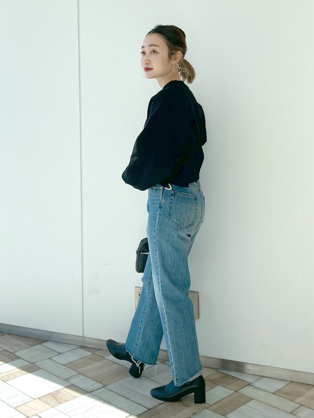 ブルー系のデニムパンツ、ブラック系のニット/セーター、ブラック系のボストンバッグを着用したレディースの冬コーディネートの3枚目の写真