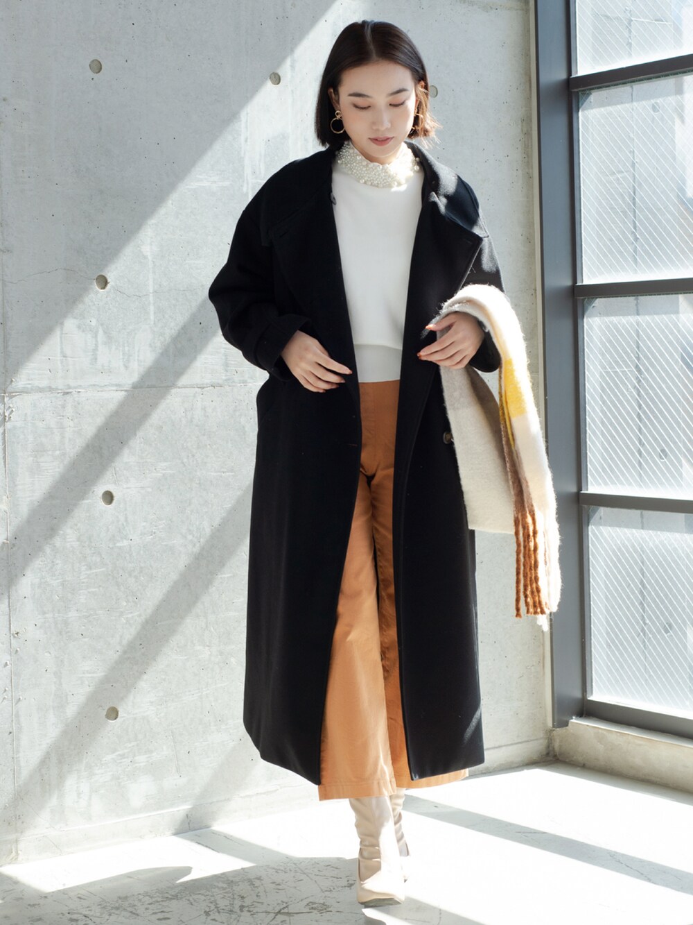 ブラック系のステンカラーコート、イエロー系のマフラーを着用したレディースの秋コーディネートの2枚目の写真