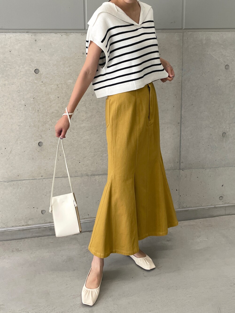 イエロー系のデニムスカート、ホワイト系のベスト、ホワイト系のパンプスを着用したレディースの春コーディネートの4枚目の写真