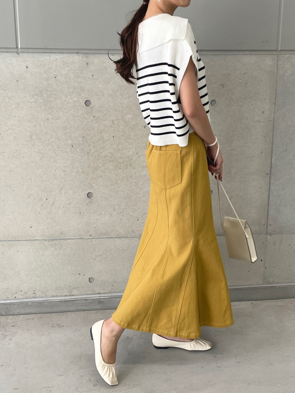 イエロー系のデニムスカート、ホワイト系のベスト、ホワイト系のパンプスを着用したレディースの春コーディネートの2枚目の写真