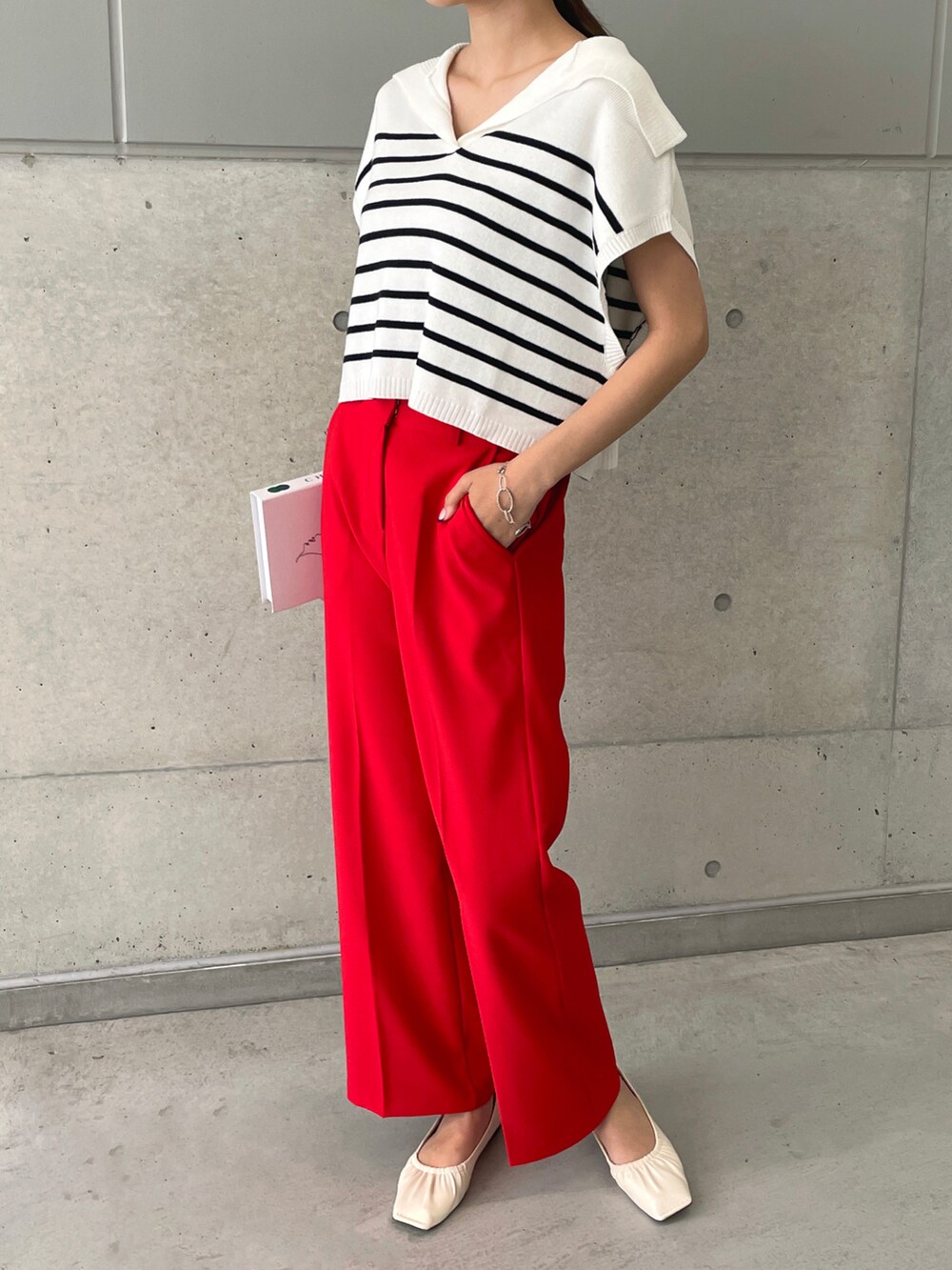 レッド系のスラックス、ホワイト系のパンプス、ホワイト系のベストを着用したレディースの春コーディネートの2枚目の写真