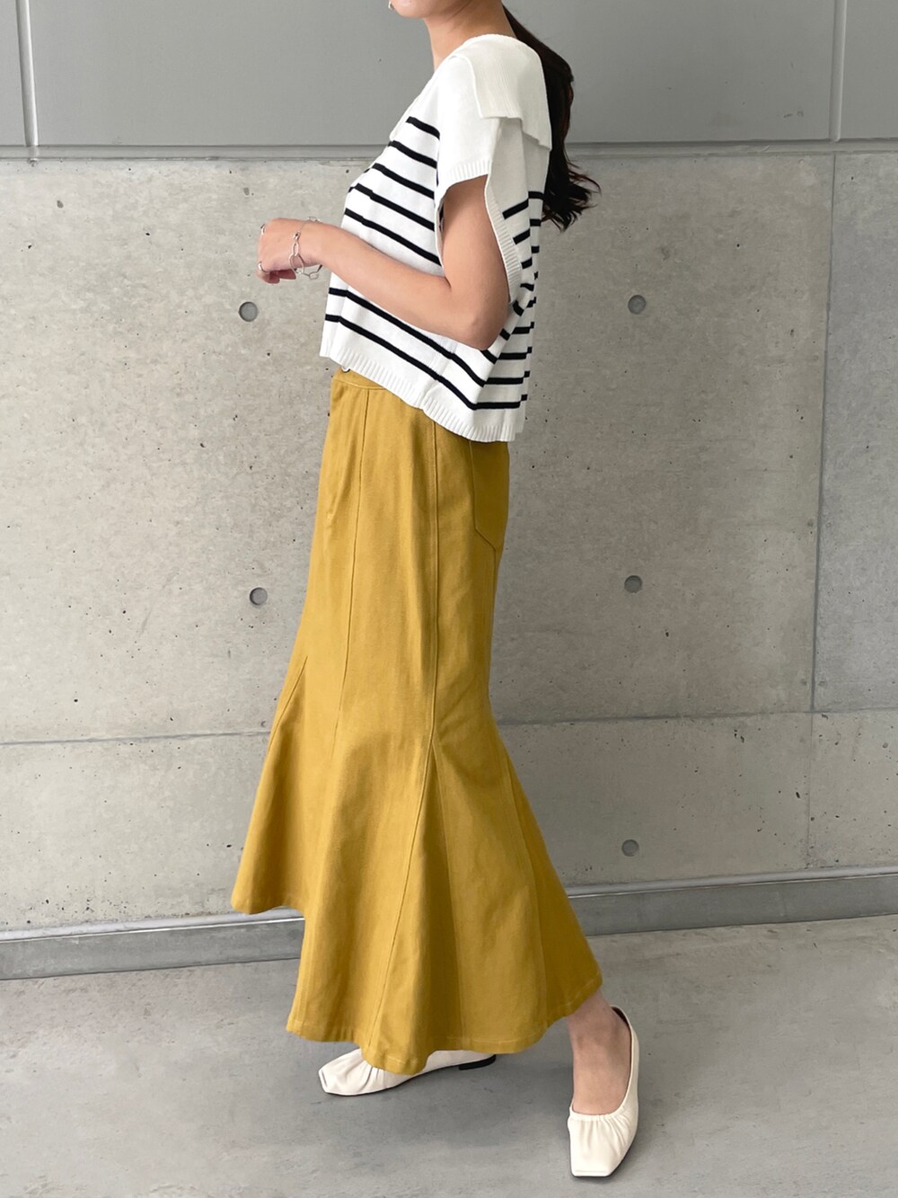 イエロー系のデニムスカート、ホワイト系のベスト、ホワイト系のパンプスを着用したレディースの春コーディネートの3枚目の写真