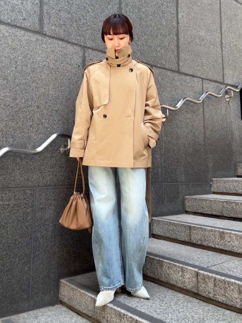 ベージュ系のトレンチコート、ブラウン系のショルダーバッグ、ブルー系のデニムパンツを着用したレディースの冬コーディネートの2枚目の写真