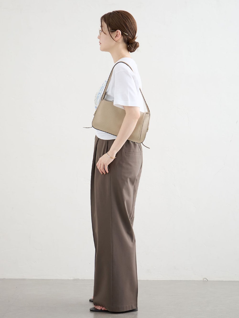 ブラウン系のスラックス、ホワイト系のTシャツ/カットソー、ブラック系のサンダルを着用したレディースの夏コーディネートの2枚目の写真