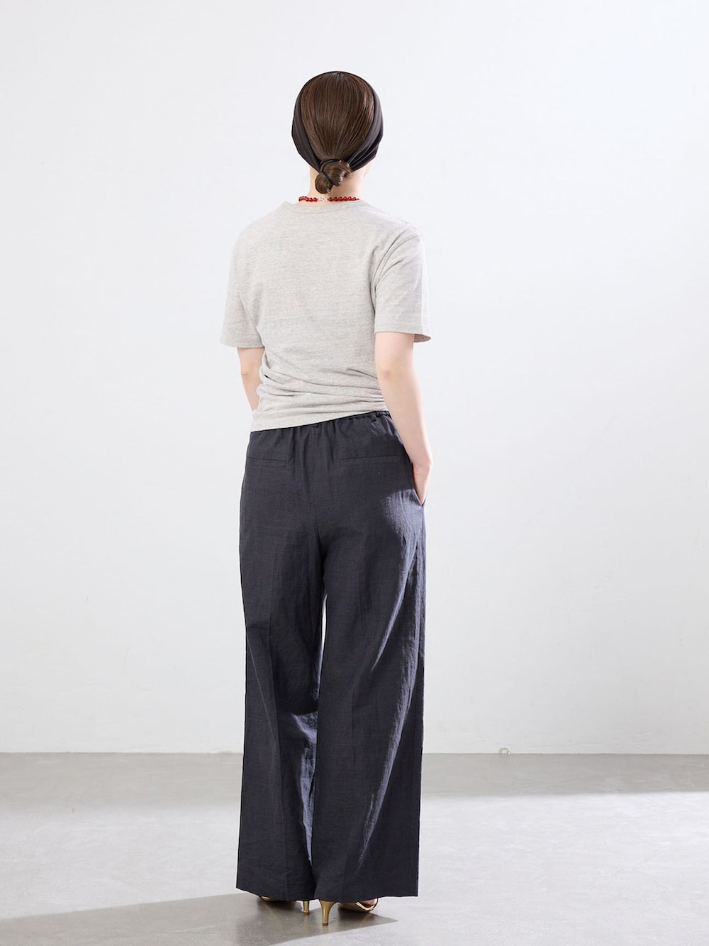 ブラック系のスラックス、グレー系のTシャツ/カットソー、ブラック系のサンダルを着用したレディースの春コーディネートの2枚目の写真