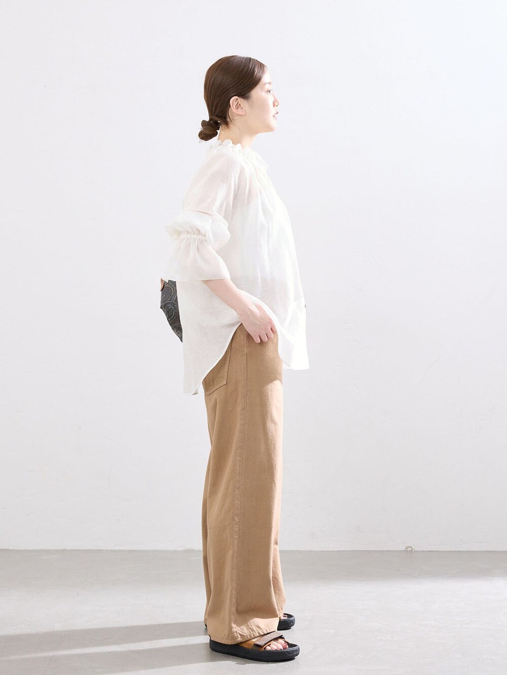 イエロー系のチノパンツ、ホワイト系のシャツ/ブラウス、ブラウン系のサンダルを着用したレディースの春コーディネートの2枚目の写真