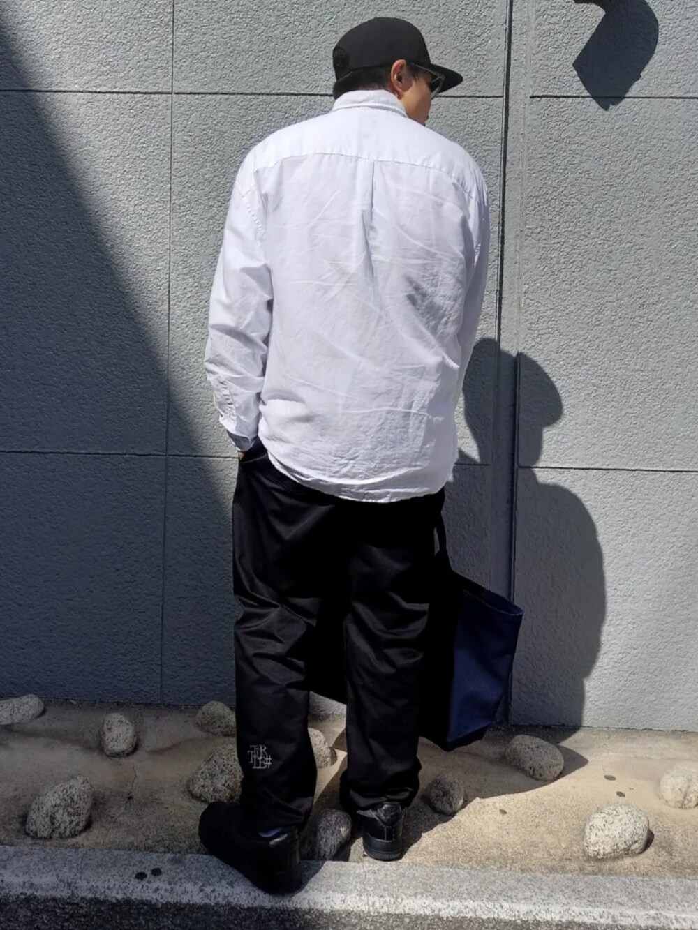 ブラック系のチノパンツ、ブルー系のトートバッグ、ブラック系のキャップを着用したメンズの春コーディネートの3枚目の写真