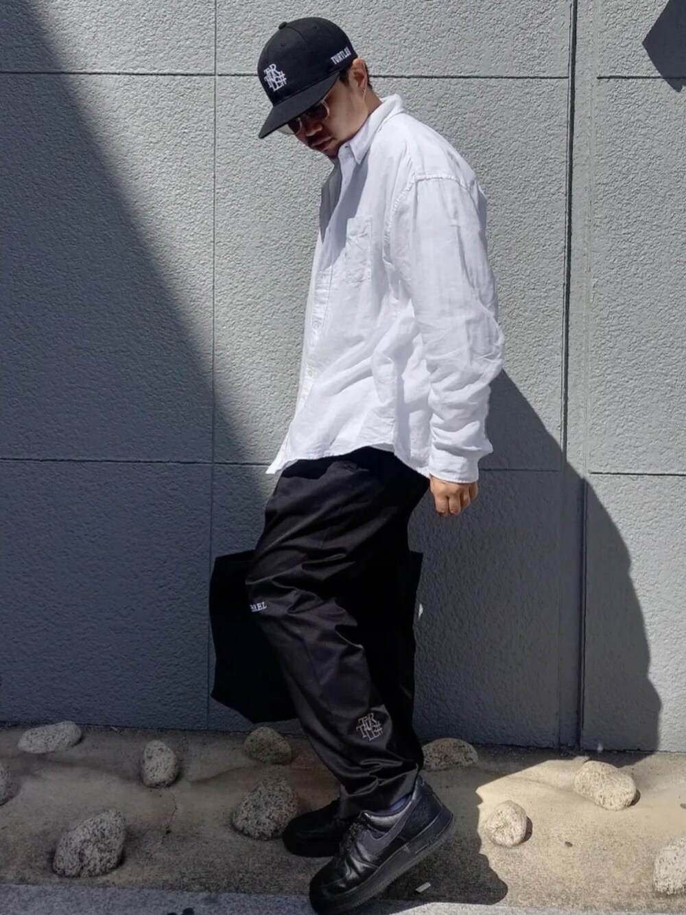 ブラック系のチノパンツ、ブルー系のトートバッグ、ブラック系のキャップを着用したメンズの春コーディネートの2枚目の写真