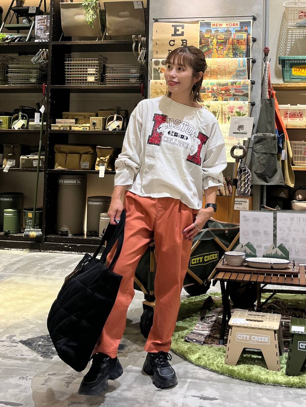 ブラック系のトートバッグ、オレンジ系のその他パンツ、ホワイト系のTシャツ/カットソーを着用したレディースの秋コーディネートの2枚目の写真