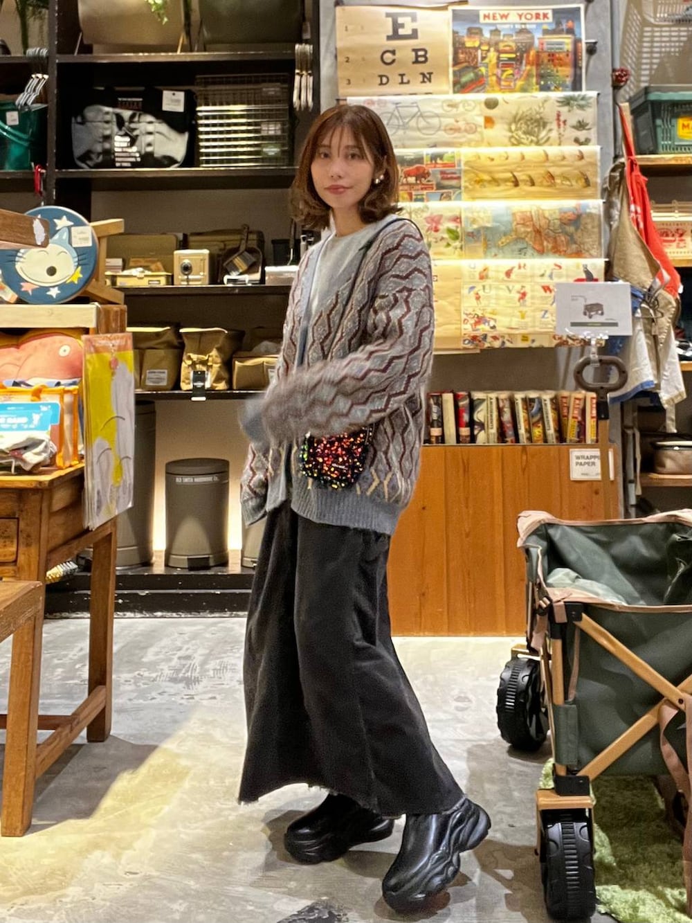 グレー系のスカート、ブルー系のカーディガン/ボレロ、ブラック系のブーツを着用したレディースの秋コーディネートの2枚目の写真