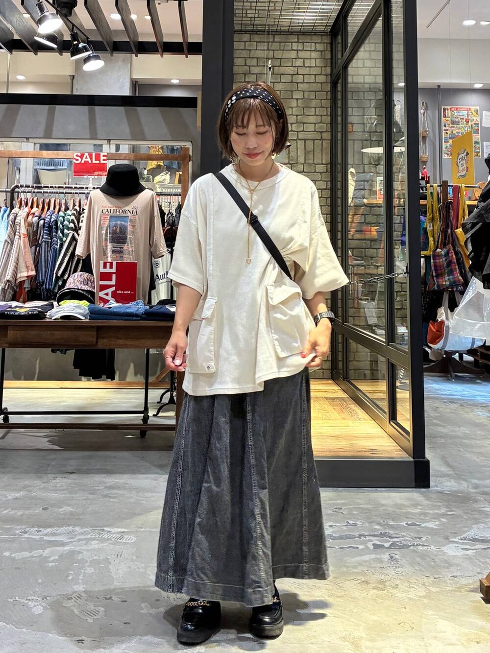 グレー系のスカート、ベージュ系のTシャツ/カットソー、ブラック系のショルダーバッグを着用したレディースの夏コーディネートの2枚目の写真