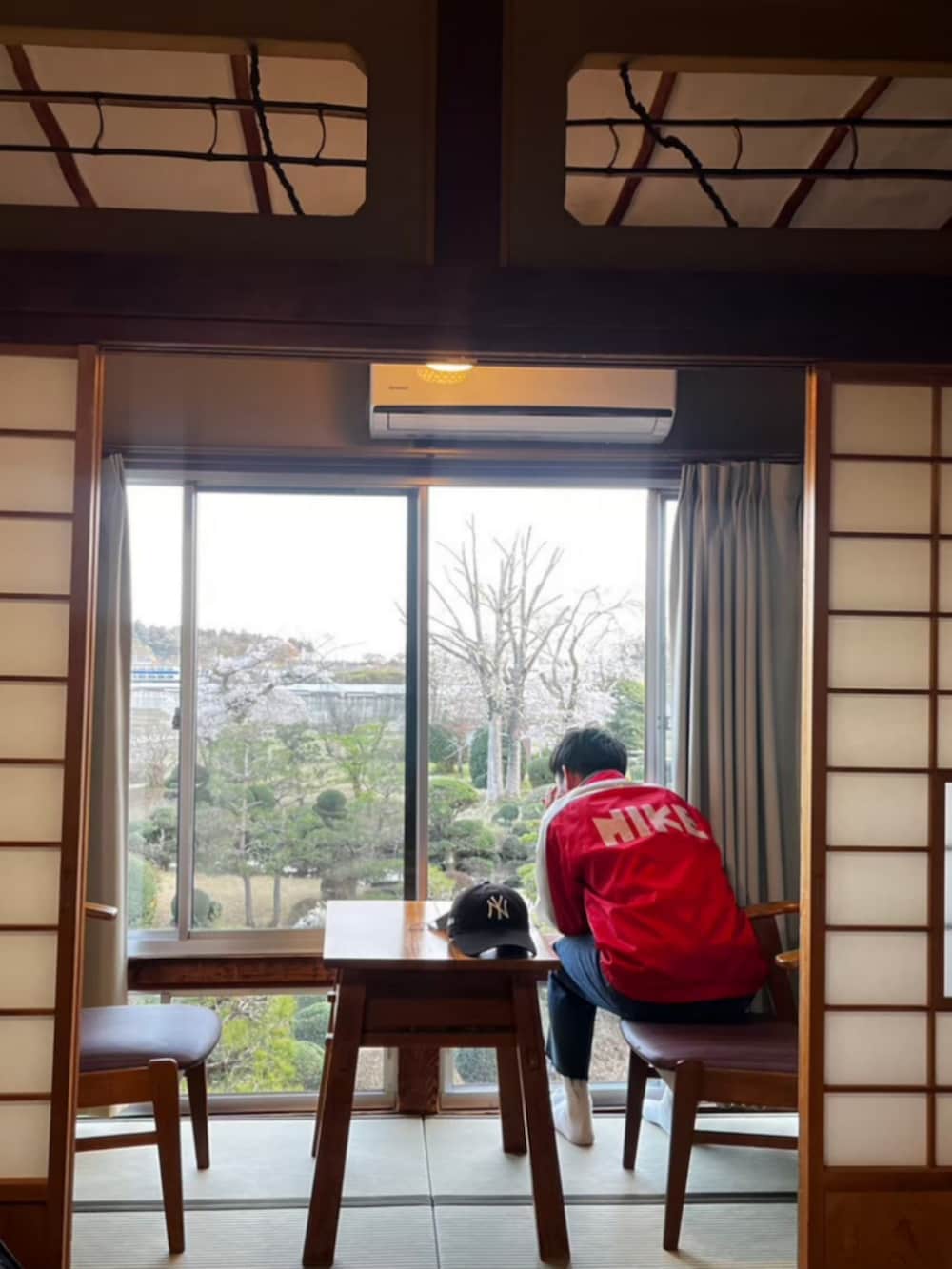 レッド系のナイロンジャケット、ブラック系のデニムパンツ、ブラック系のキャップを着用したメンズの春コーディネートの2枚目の写真