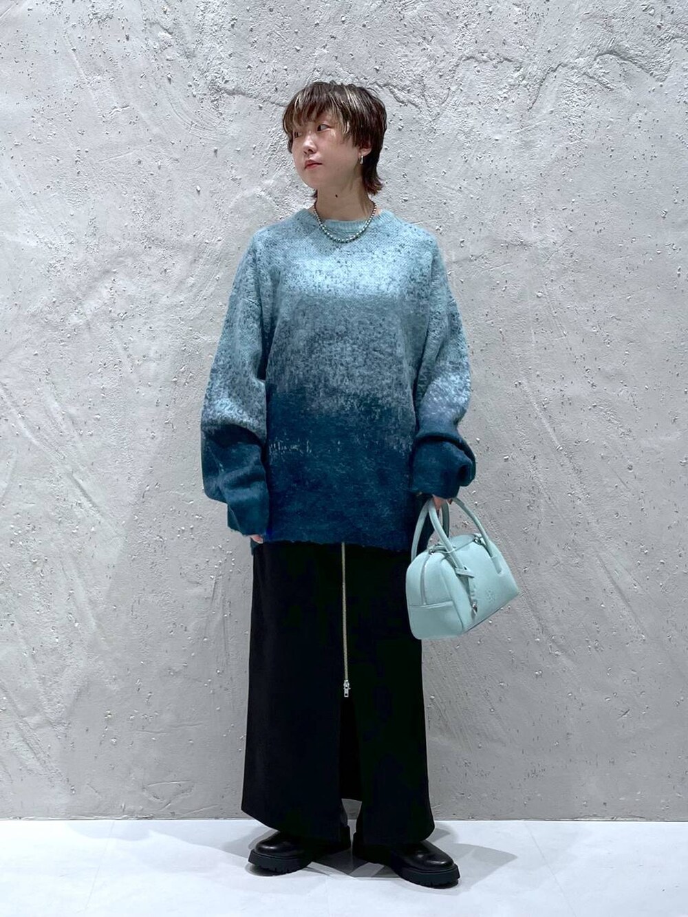 グリーン系のニット/セーター、グリーン系のボストンバッグ、ブラック系のスカートを着用したレディースの秋コーディネートの5枚目の写真