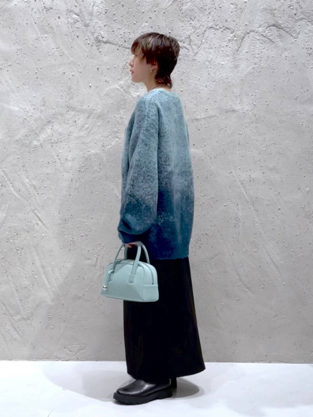 グリーン系のニット/セーター、グリーン系のボストンバッグ、ブラック系のスカートを着用したレディースの秋コーディネートの2枚目の写真