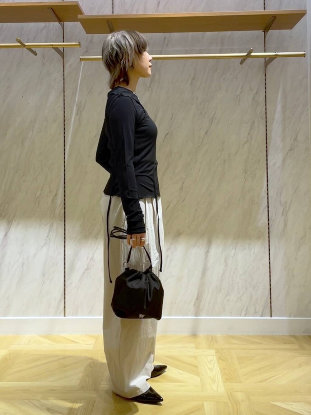 ブラック系のパンプス、ホワイト系のスラックス、ブラック系のショルダーバッグを着用したレディースの春コーディネートの2枚目の写真