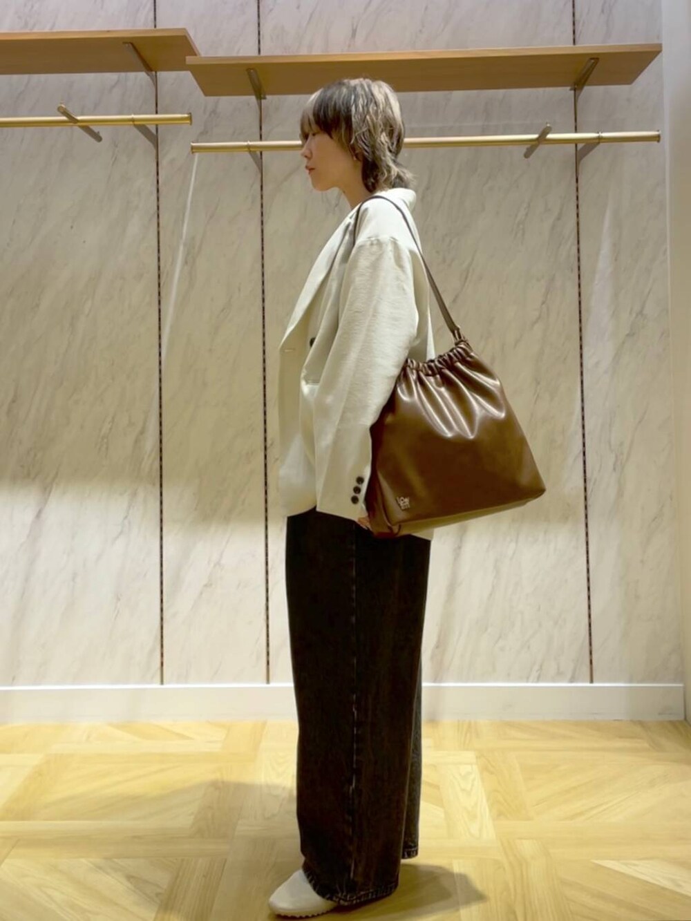 ブラウン系のショルダーバッグ、ホワイト系のテーラードジャケット、ブラック系のデニムパンツを着用したレディースの春コーディネートの2枚目の写真