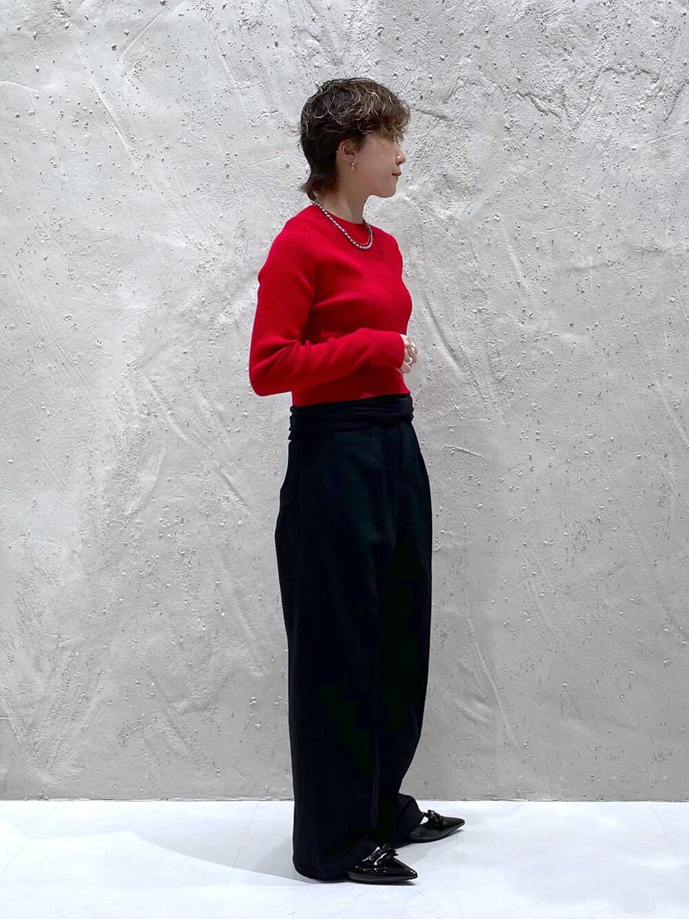 ブラック系のパンプス、レッド系のニット/セーター、ブラック系のデニムパンツを着用したレディースの秋コーディネートの4枚目の写真