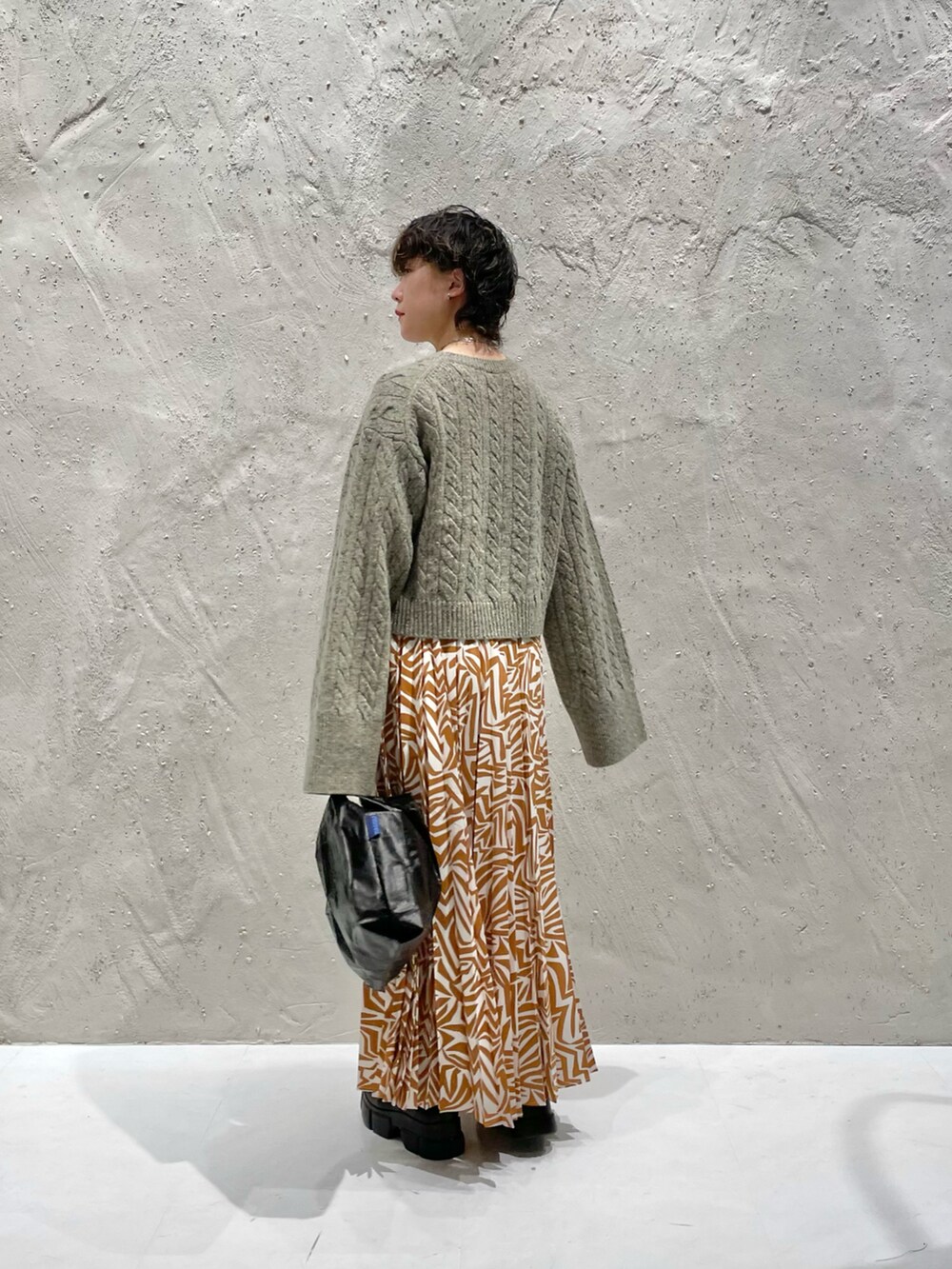 ブラウン系のニット/セーター、ブラウン系のスカート、ブラック系のブーツを着用したレディースの秋コーディネートの2枚目の写真