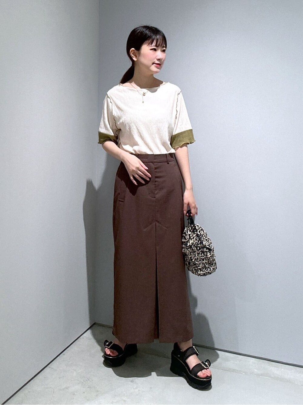 ホワイト系のTシャツ/カットソー、ブラウン系のスカート、ブラック系のハンドバッグを着用したレディースの夏コーディネートの2枚目の写真