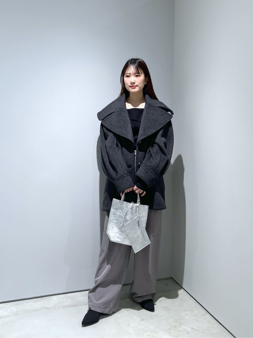 グレー系のチェスターコート、ブラック系のニット/セーター、グレー系のその他パンツを着用したレディースの冬コーディネートの2枚目の写真