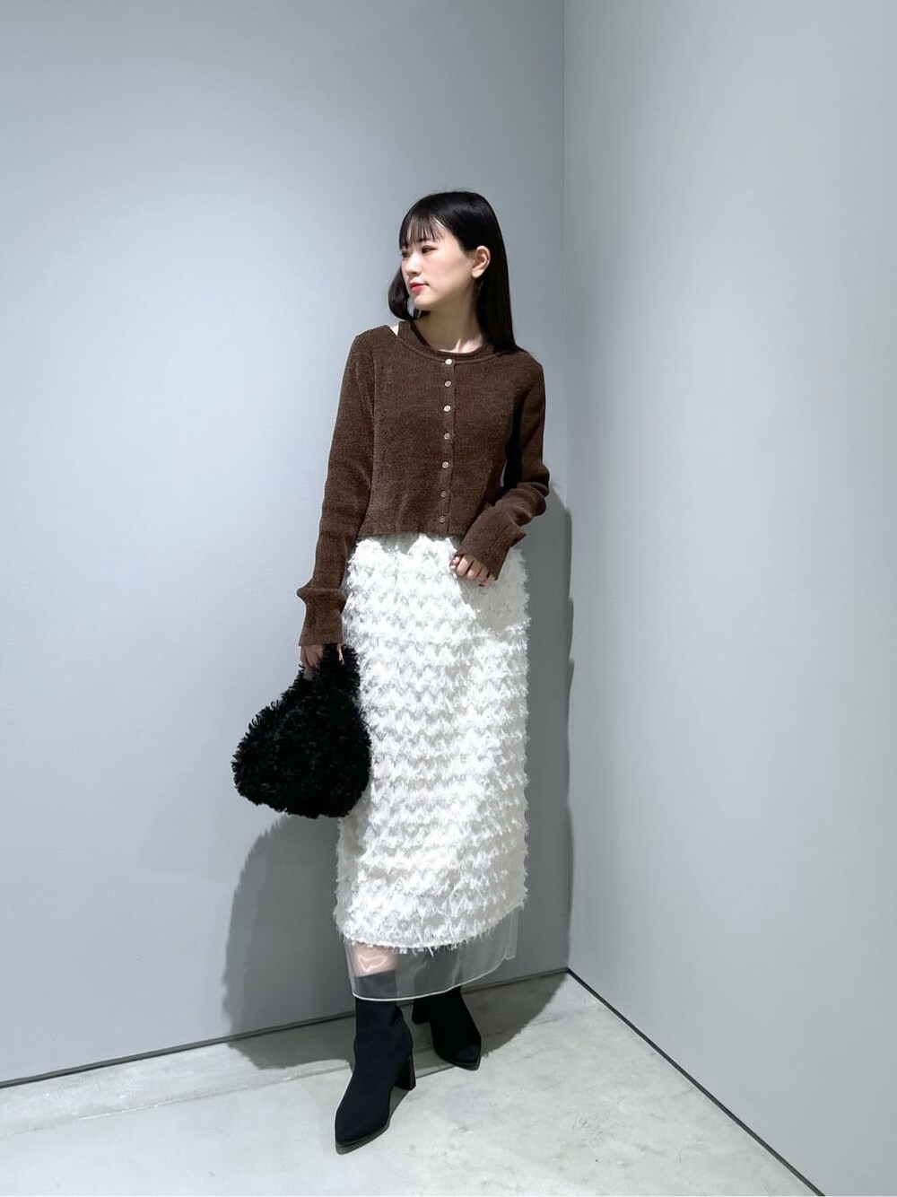 ブラウン系のニット/セーター、ホワイト系のスカート、ブラック系のハンドバッグを着用したレディースの冬コーディネートの2枚目の写真