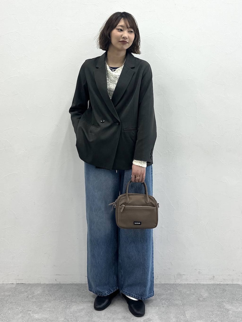 ブラウン系のハンドバッグ、グレー系のテーラードジャケット、ブルー系のデニムパンツを着用したレディースの春コーディネートの2枚目の写真