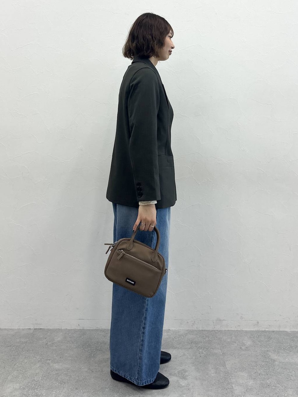 ブラウン系のハンドバッグ、グレー系のテーラードジャケット、ブルー系のデニムパンツを着用したレディースの春コーディネートの3枚目の写真